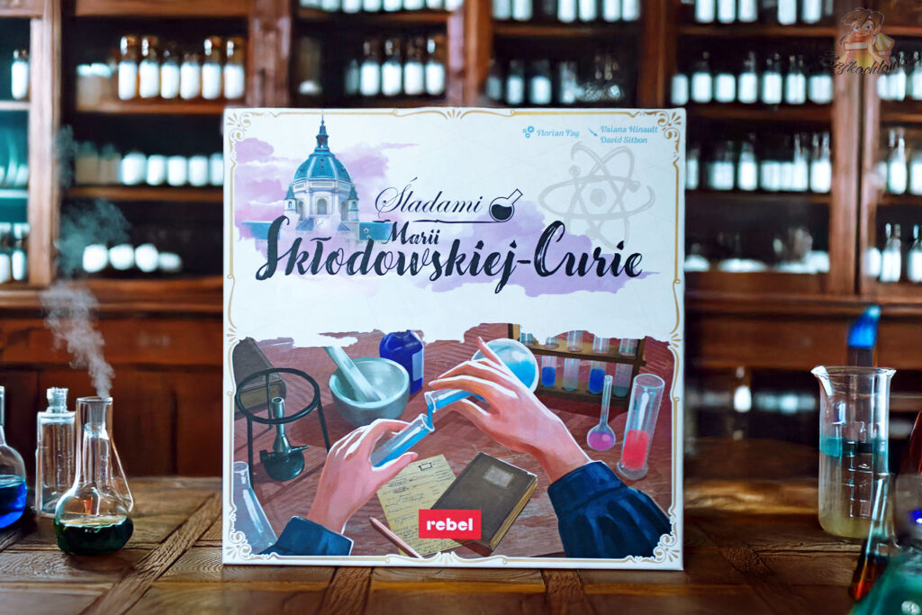 Gra planszowa „Śladami Marii Skłodowskiej-Curie” Rebel – pudełko na tle retro pracowni chemicznej