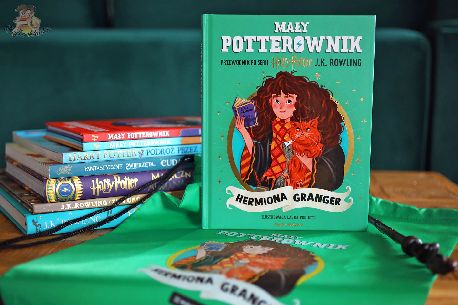 „Mały potterownik: Hermiona Granger” – okładka na tle zielonego worka, obok stos książek z uniwersum Harry’ego Pottera