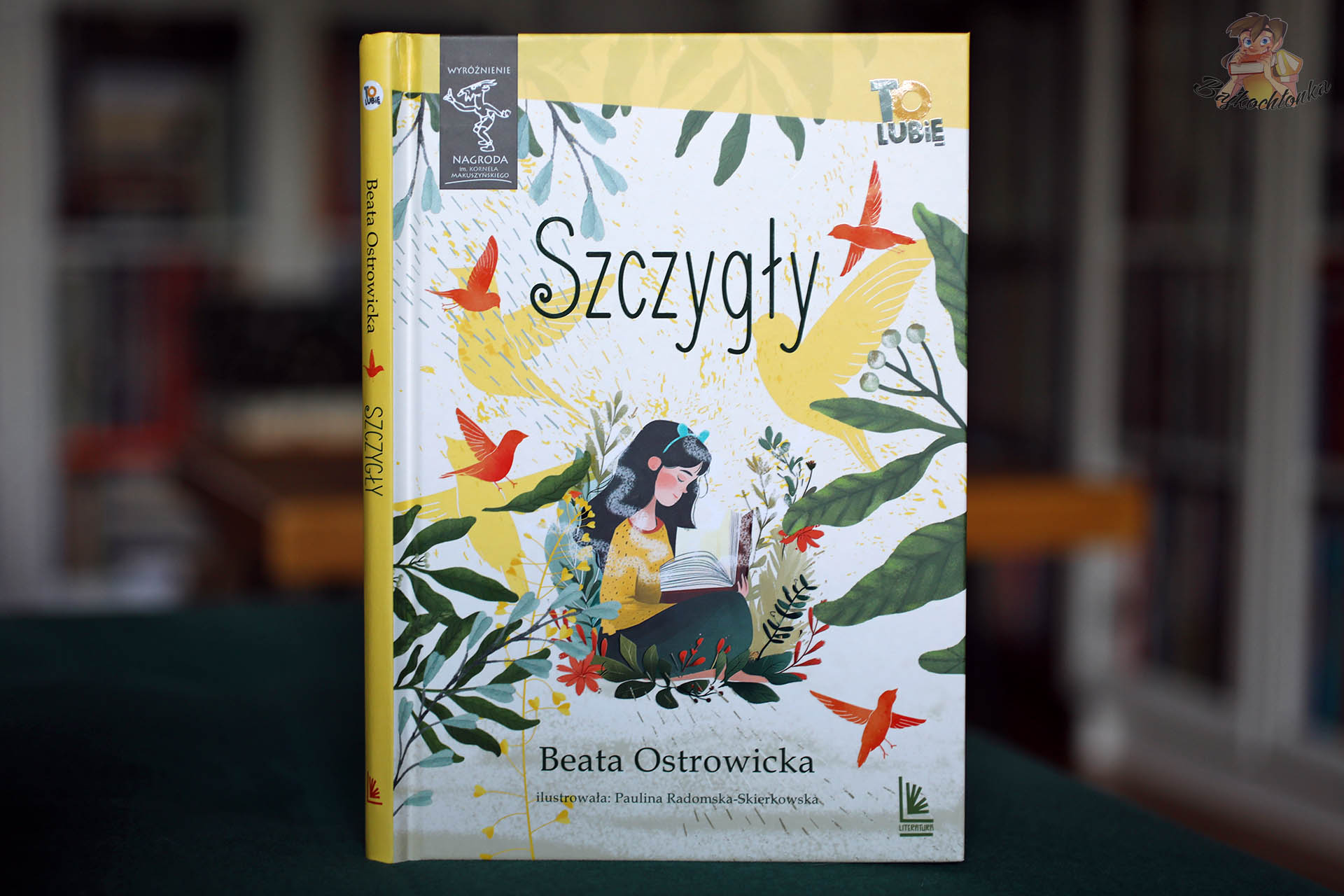 Okładka i grzbiet książki „Szczygły” Beaty Ostrowickiej, Wydawnictwo Literatura; ilustracje Pauliny Radomskiej-Skierkowskiej.