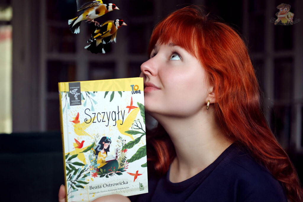 Osoba z rudymi włosami trzyma książkę „Szczygły”; nad okładką lecą dwa szczygły w fotomontażu.