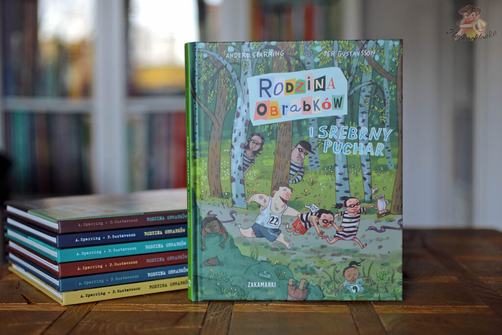 Okładka „Rodzina Obrabków i srebrny puchar” na tle stosu poprzednich tomów serii – książka dla dzieci, Zakamarki