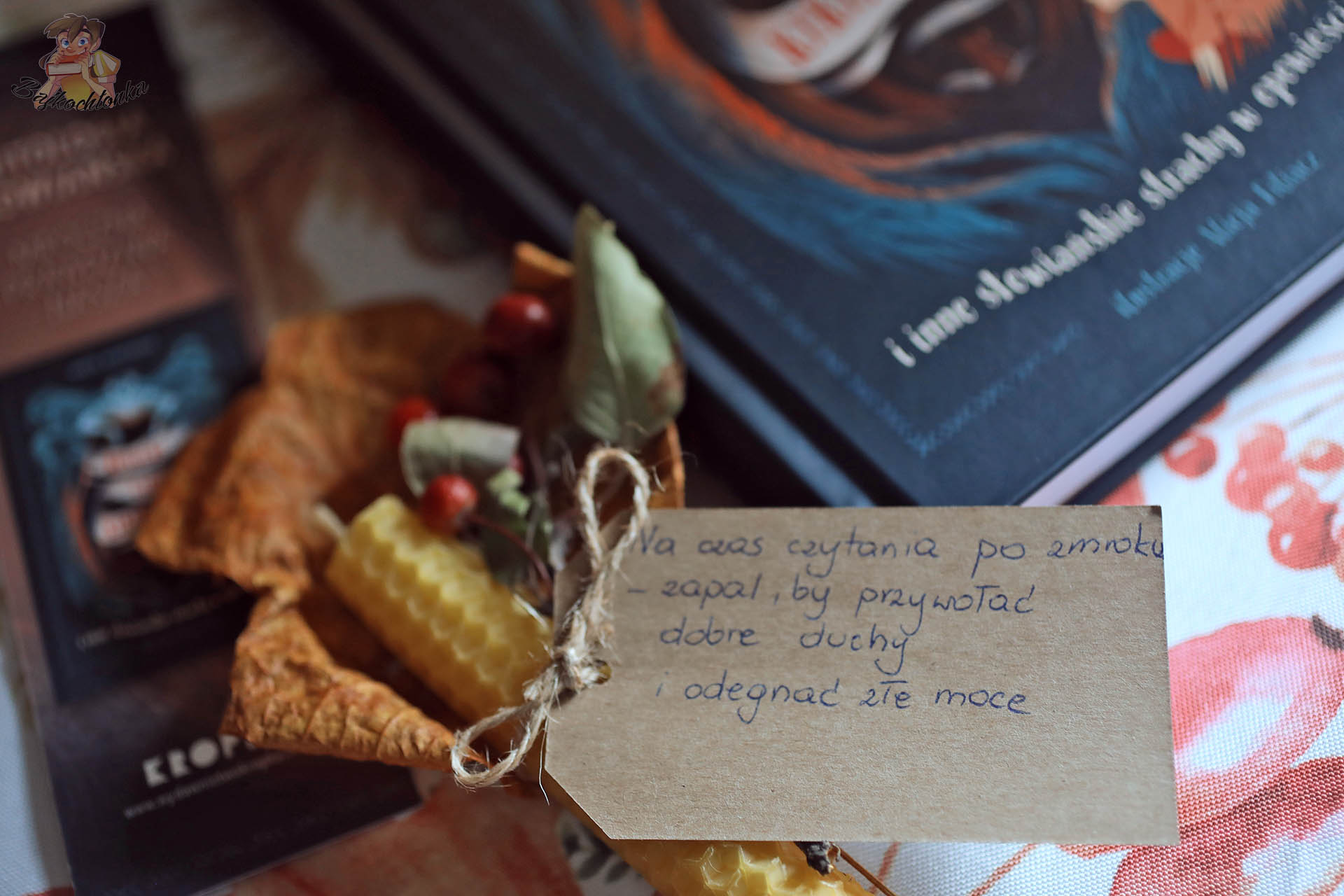 Jesienny rekwizyt do lektury: woskowa świeca i bilecik obok książki „Rusałki, licha, kikimory…”.