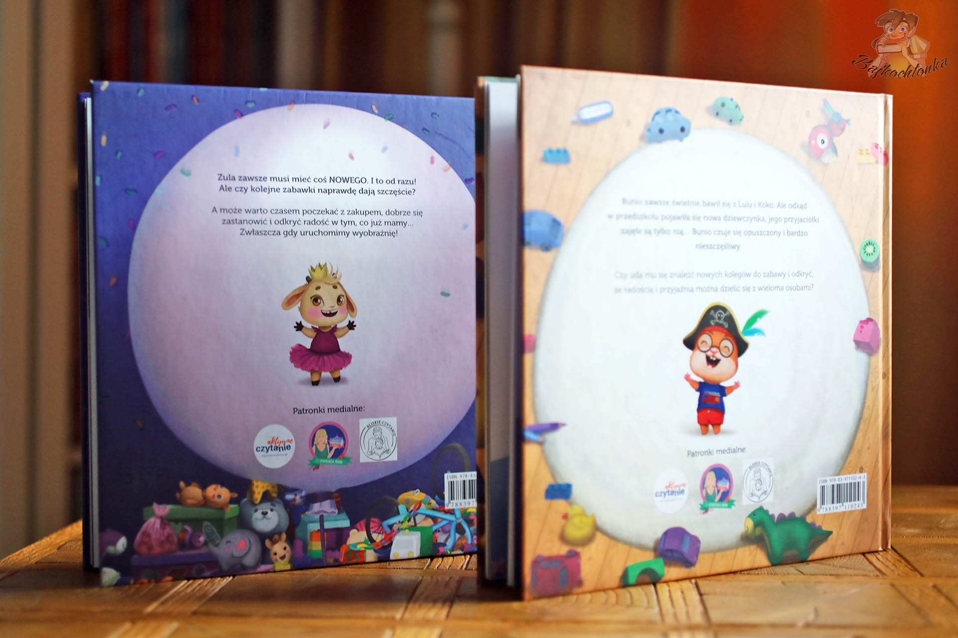 Zdjęcie tylnych okładek dwóch książek z Doliny Tumilu – krótkie opisy fabuł, bohaterowie i patronaty medialne, recenzja serii dla maluchów.