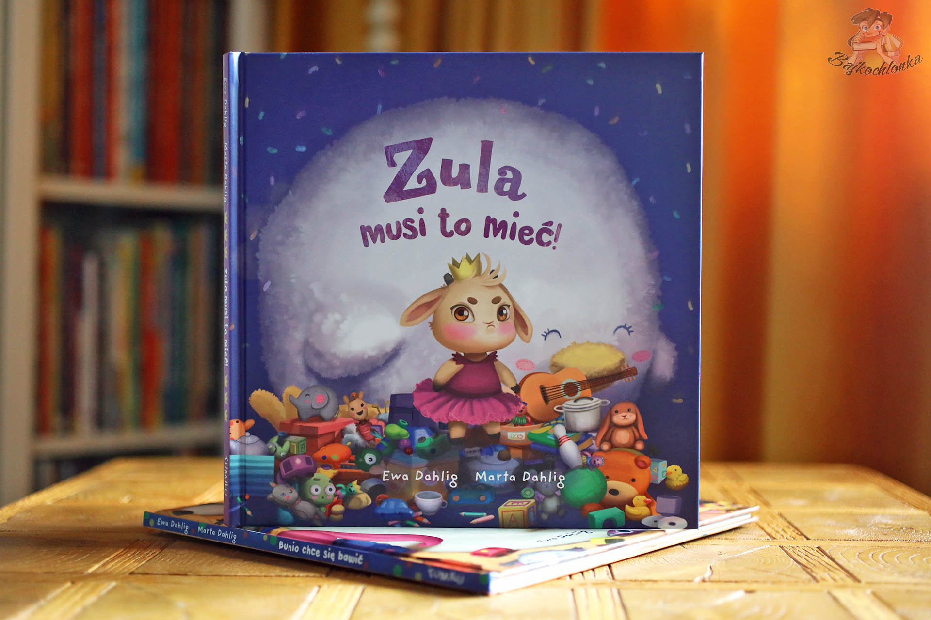 Książka „Zula musi to mieć!” z bohaterką pośród zabawek – opowieść o potrzebach, cierpliwości i radości z tego, co już mamy.