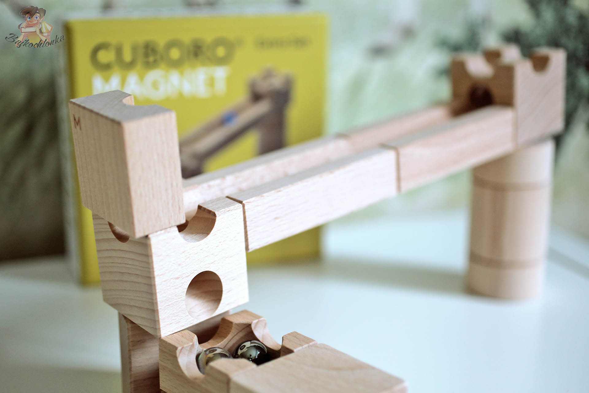 Drewniany tor kulkowy Cuboro Magnet z bukowych klocków, fragment zjazdu z kulkami na tle żółtego pudełka zestawu