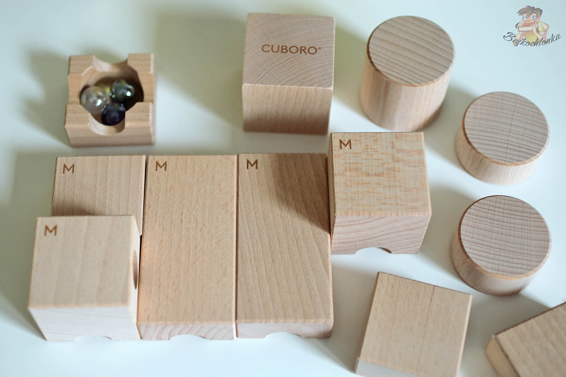 Rozłożone elementy zestawu Cuboro Magnet, bukowe klocki i miseczka z kulkami na białym stole