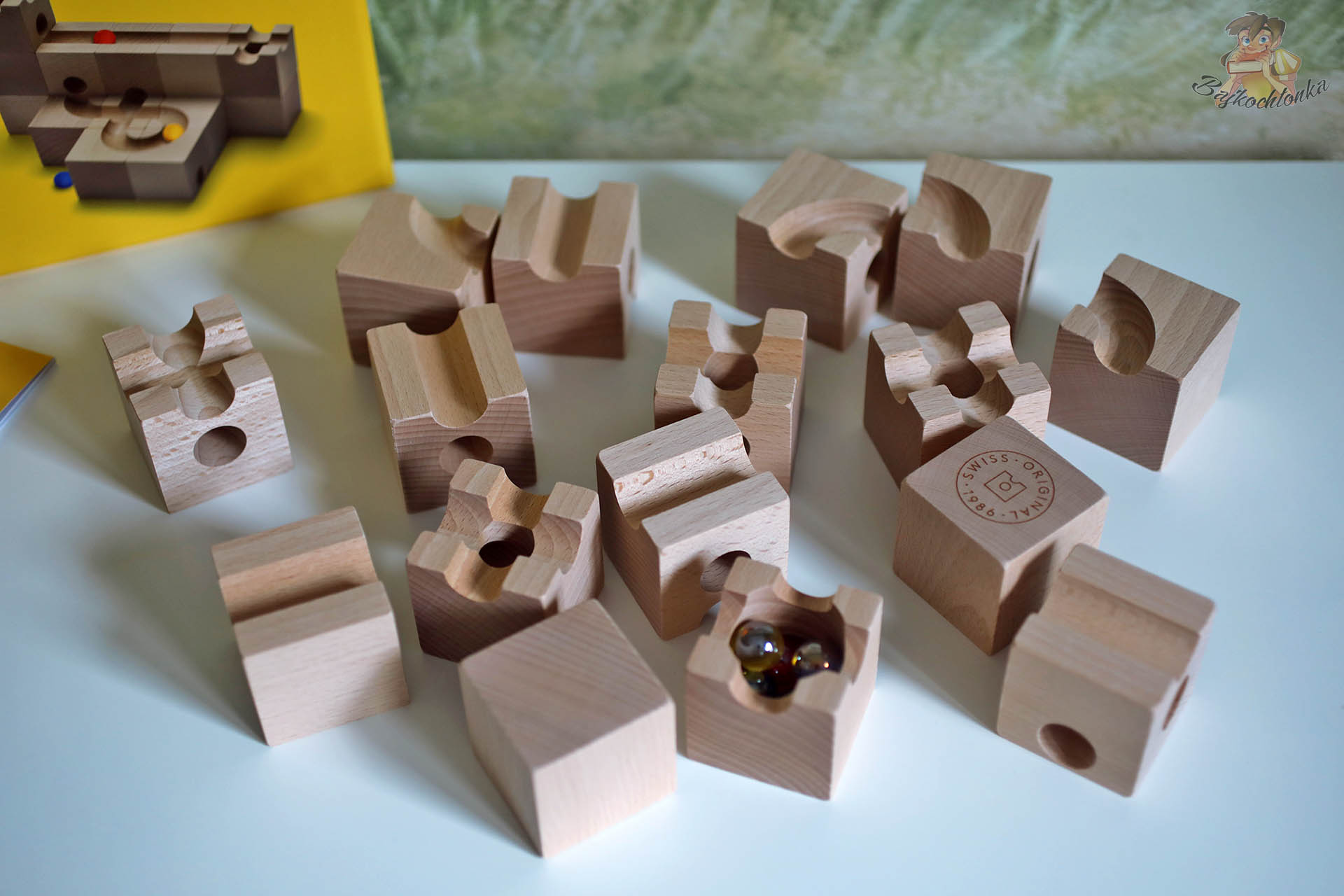 Rozłożone bukowe klocki systemu Cuboro Magnet z różnymi wyfrezowanymi kanałami i miseczką z kulkami