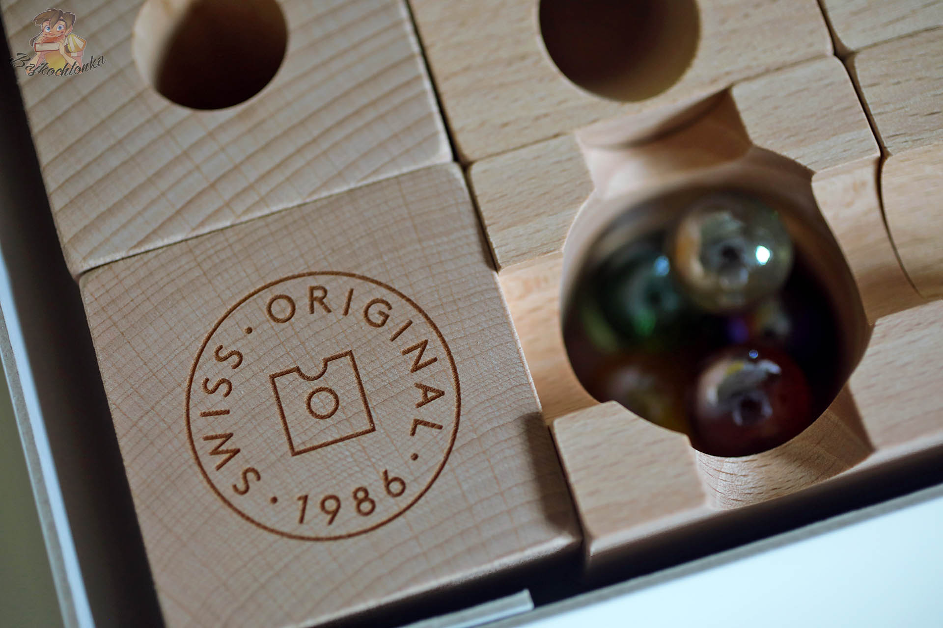 Zbliżenie na bukowy klocek Cuboro z wygrawerowanym logo Swiss Original 1986 oraz sąsiedni element z kulkami