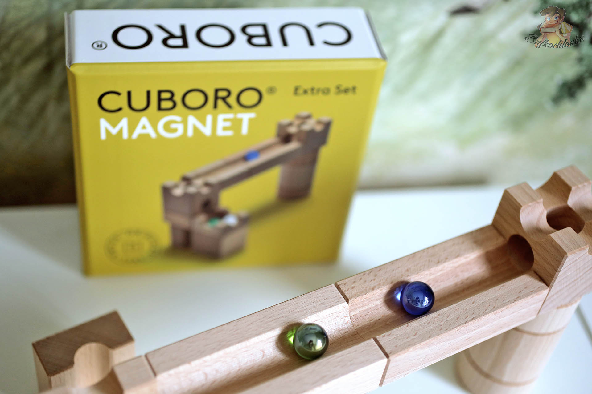 Drewniany zjazd z kolorowymi kulkami przed żółtym pudełkiem Cuboro Magnet Extra Set