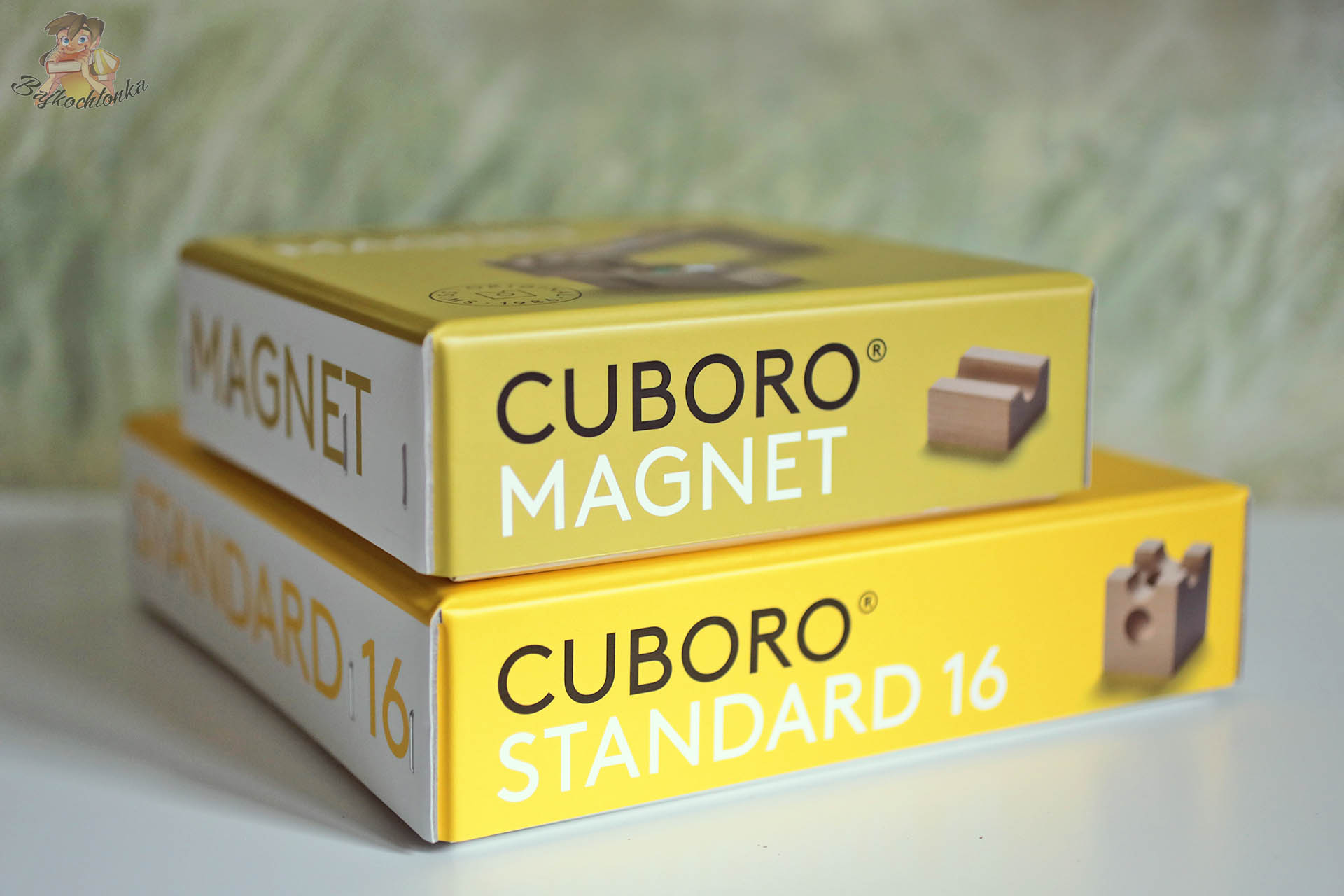Pudełka zestawów Cuboro Standard 16 i Cuboro Magnet ułożone w stos, drewniany tor kulkowy