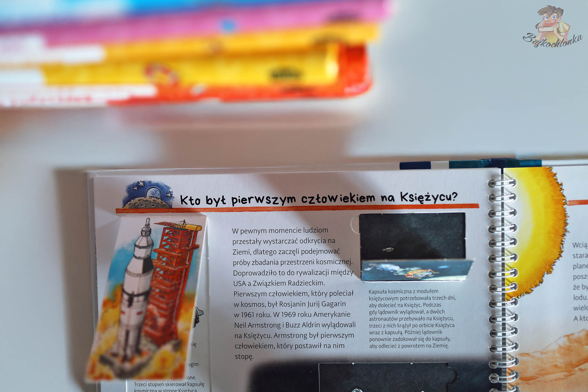 Rozkładówka z książki z okienkami Odkrywcy i podróżnicy z serii Dlaczego? Kiedy? Jak? – rakieta startująca w kosmos i tekst o pierwszym człowieku na Księżycu.