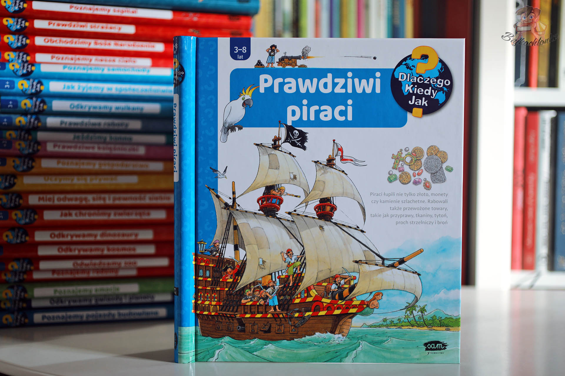 Okładka książki z okienkami Prawdziwi piraci z serii Dlaczego? Kiedy? Jak? – duży piracki żaglowiec na morzu, załoga na pokładzie, papuga i monety symbolizujące skarb.