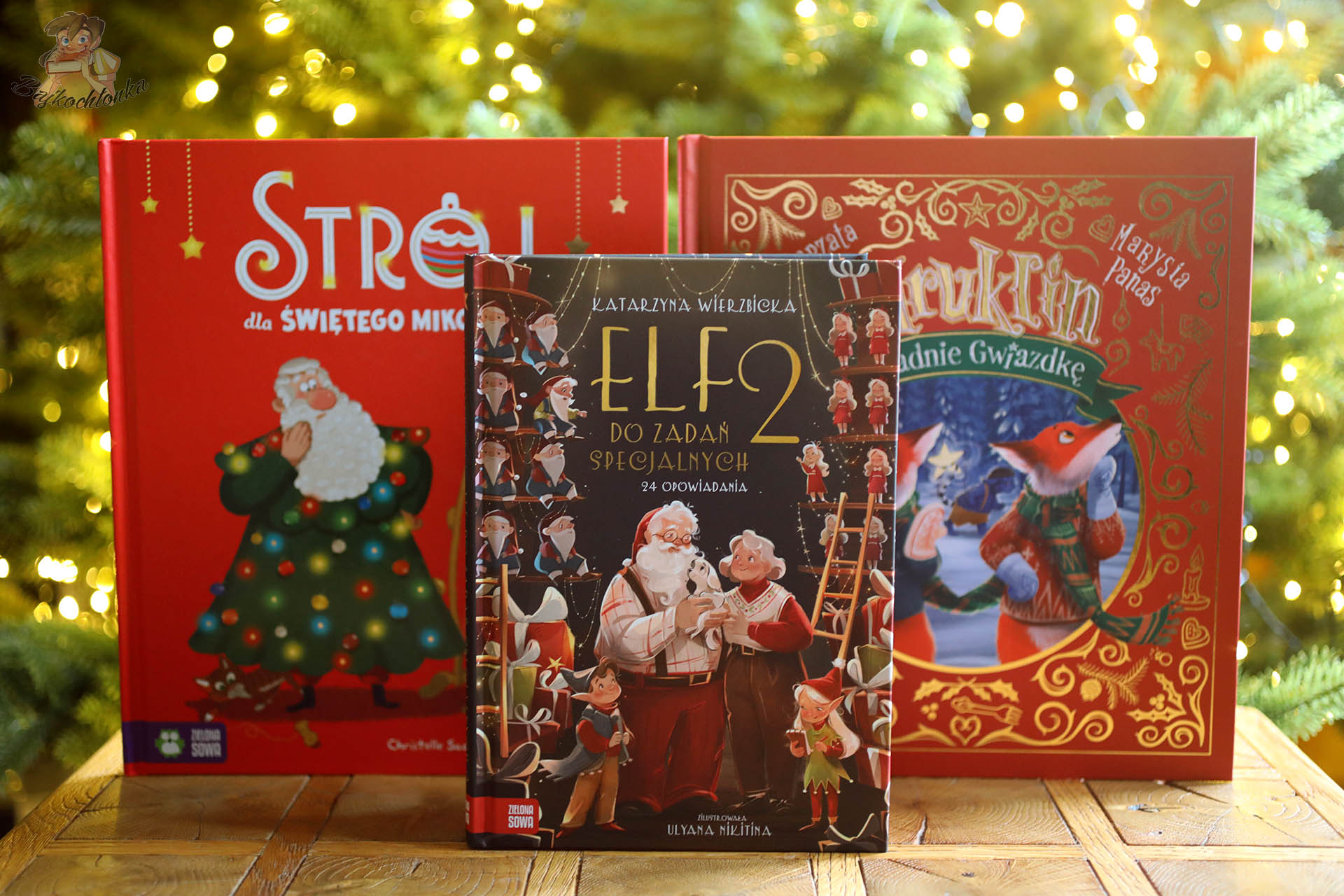 Trzy świąteczne książki od Zielonej Sowy: Strój dla Świętego Mikołaja, Elf do zadań specjalnych 2 i Mruklin kradnie Gwiazdkę ustawione przed choinką
