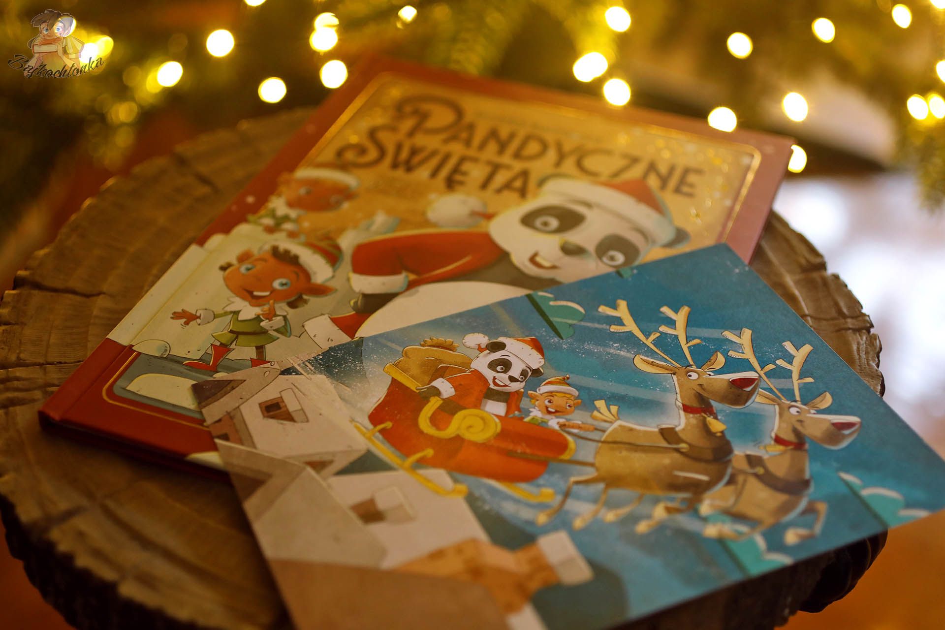 Książka Pandyczne święta i kartka z pandą w saniach na drewnianym pieńku