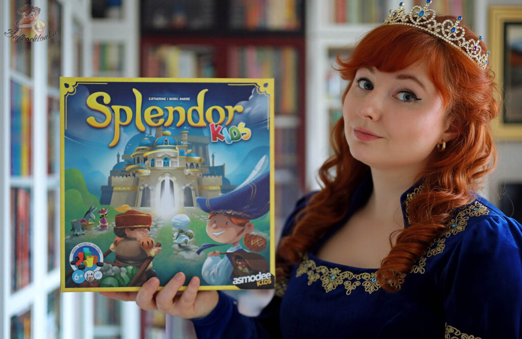 Bajkochłonka w sukni i koronie trzyma pudełko gry Splendor Kids