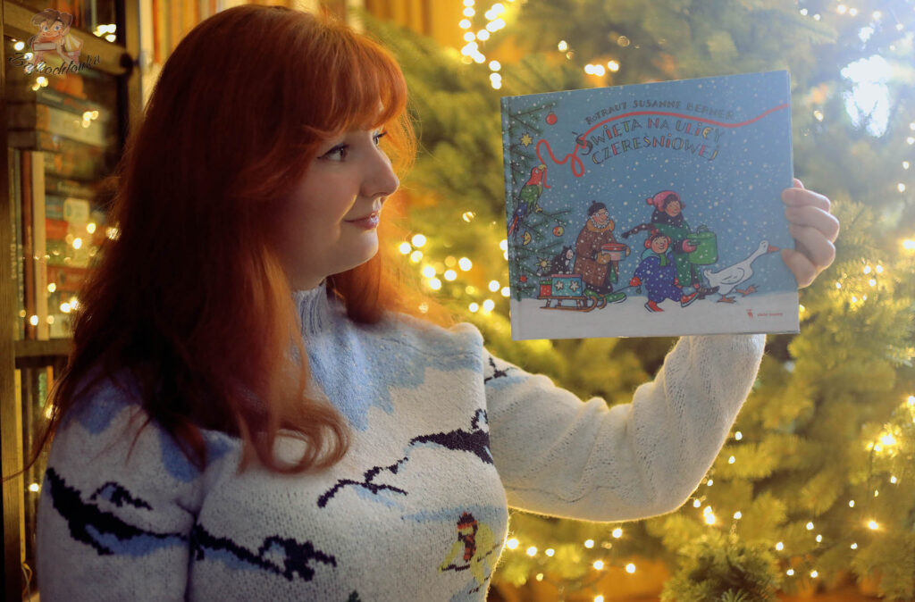 Bajkochłonka trzyma książkę Święta na ulicy Czereśniowej na tle świątecznej choinki