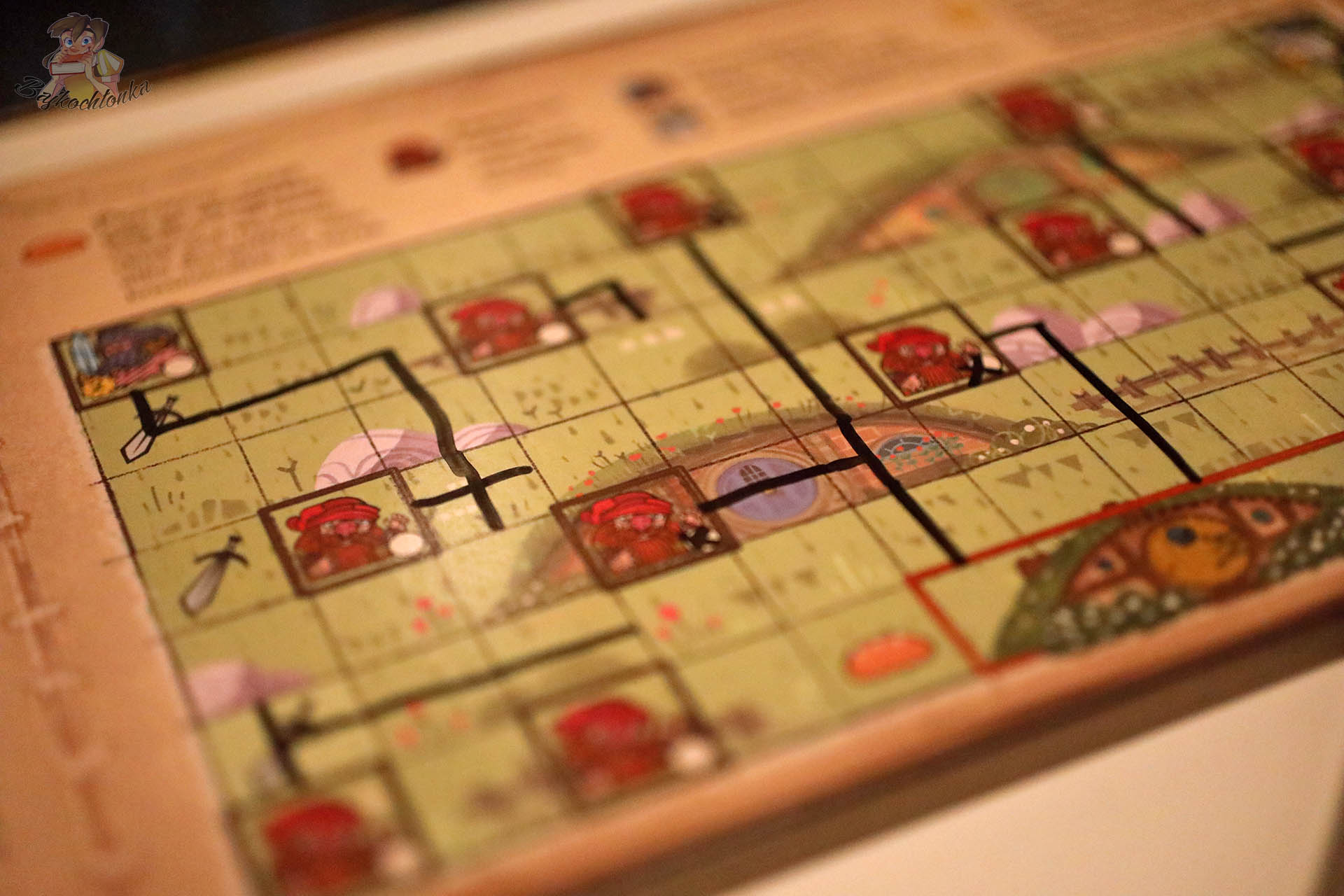 Zbliżenie na książkową planszę gry „Hobbit: Tam i z powrotem” przedstawiającą Hobbiton z zaznaczonymi trasami