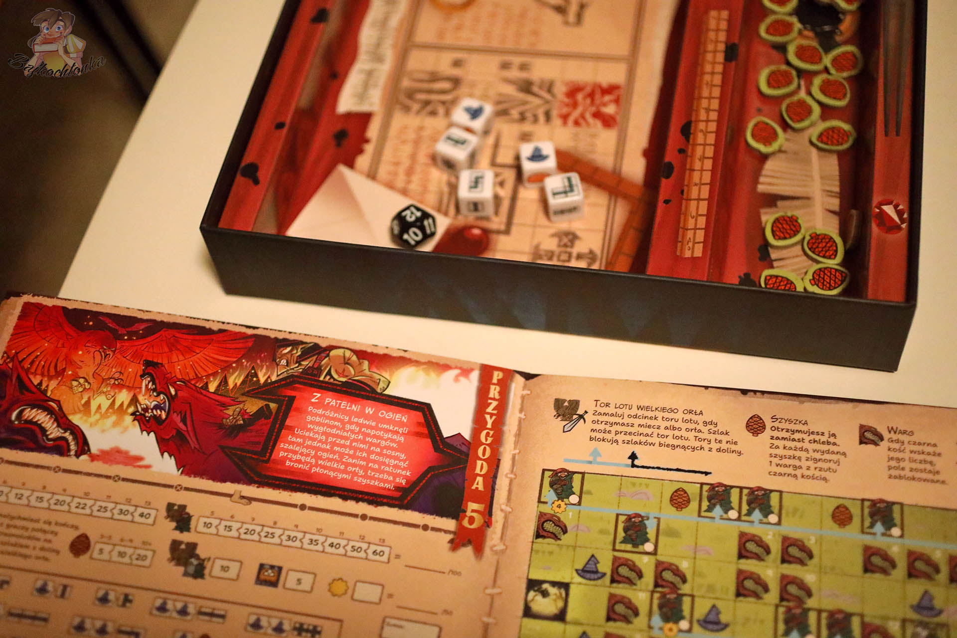 Rozłożona plansza przygody oraz wnętrze pudełka z kostkami i żetonami gry „Hobbit: Tam i z powrotem”