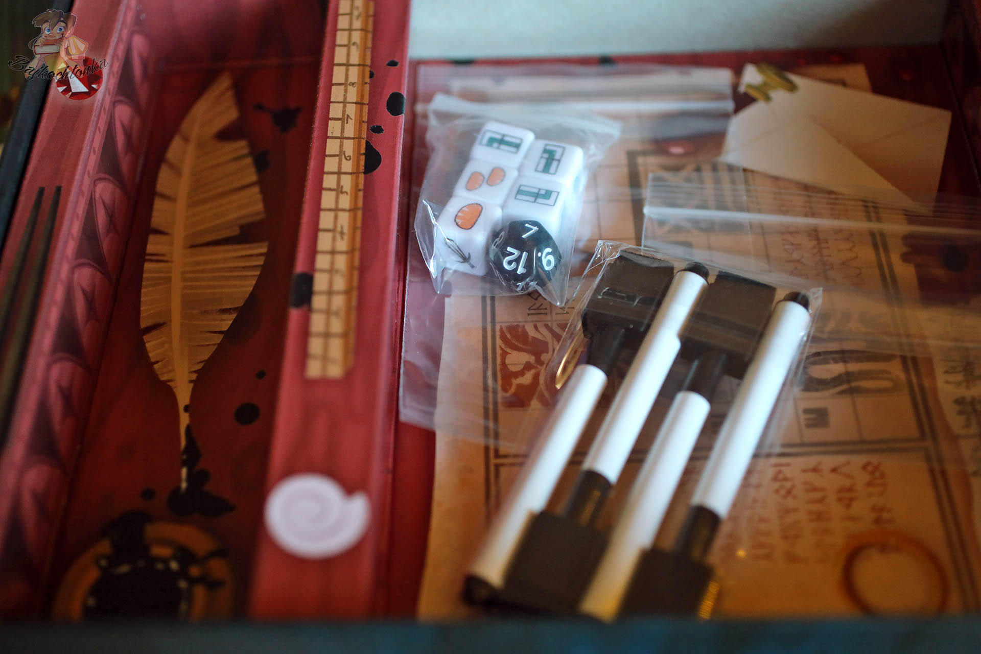 Wnętrze pudełka gry „Hobbit: Tam i z powrotem” z czterema mazakami, kostkami i ilustracją pióra na wyprasce