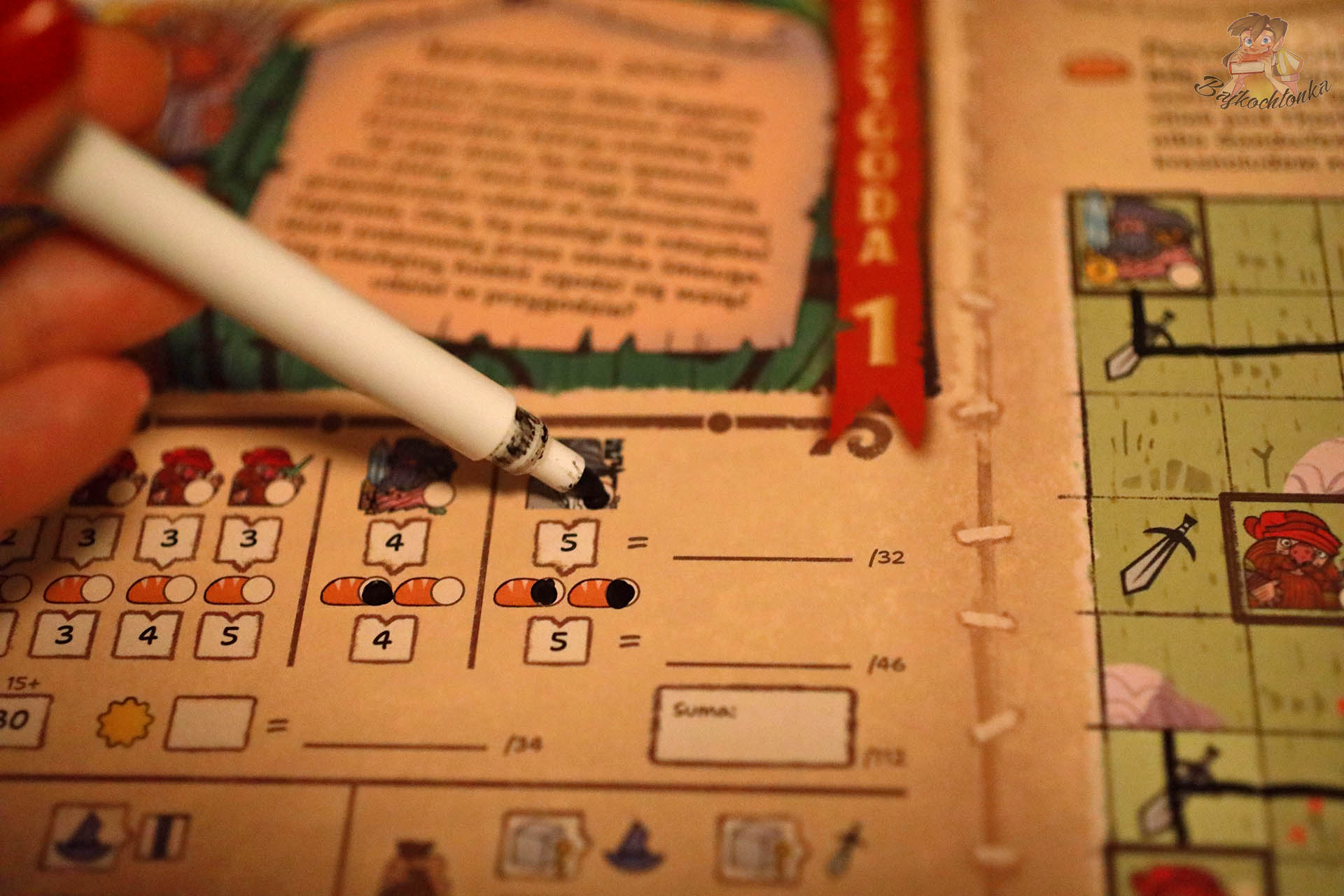 Ręka gracza zaznaczająca wyniki ścieralnym mazakiem na planszy przygody w grze „Hobbit: Tam i z powrotem”