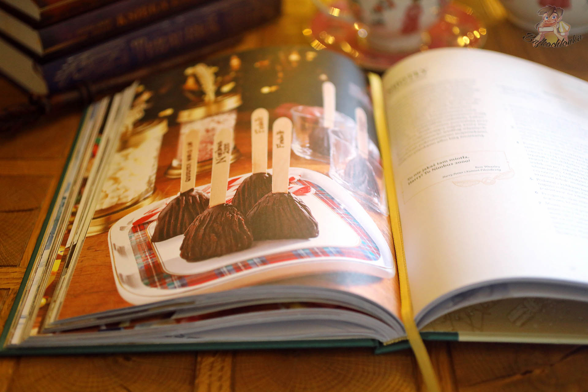 Środek Harry Potter. Oficjalna świąteczna książka kucharska z fotografią czekoladowych deserów ustawionych na tacy, w tle filiżanka i świąteczny wystrój stołu.