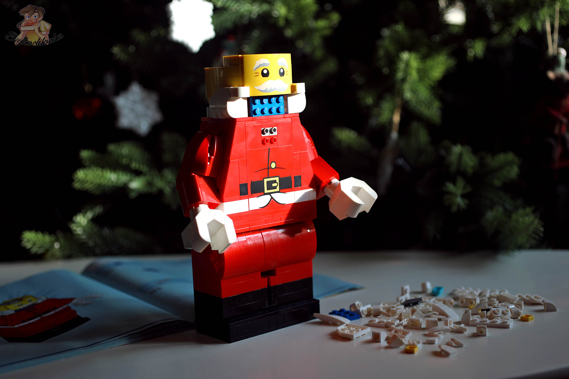 Powiększona minifigurka Świętego Mikołaja LEGO 40820 w trakcie budowy, bez założonej brody, na tle świątecznej choinki