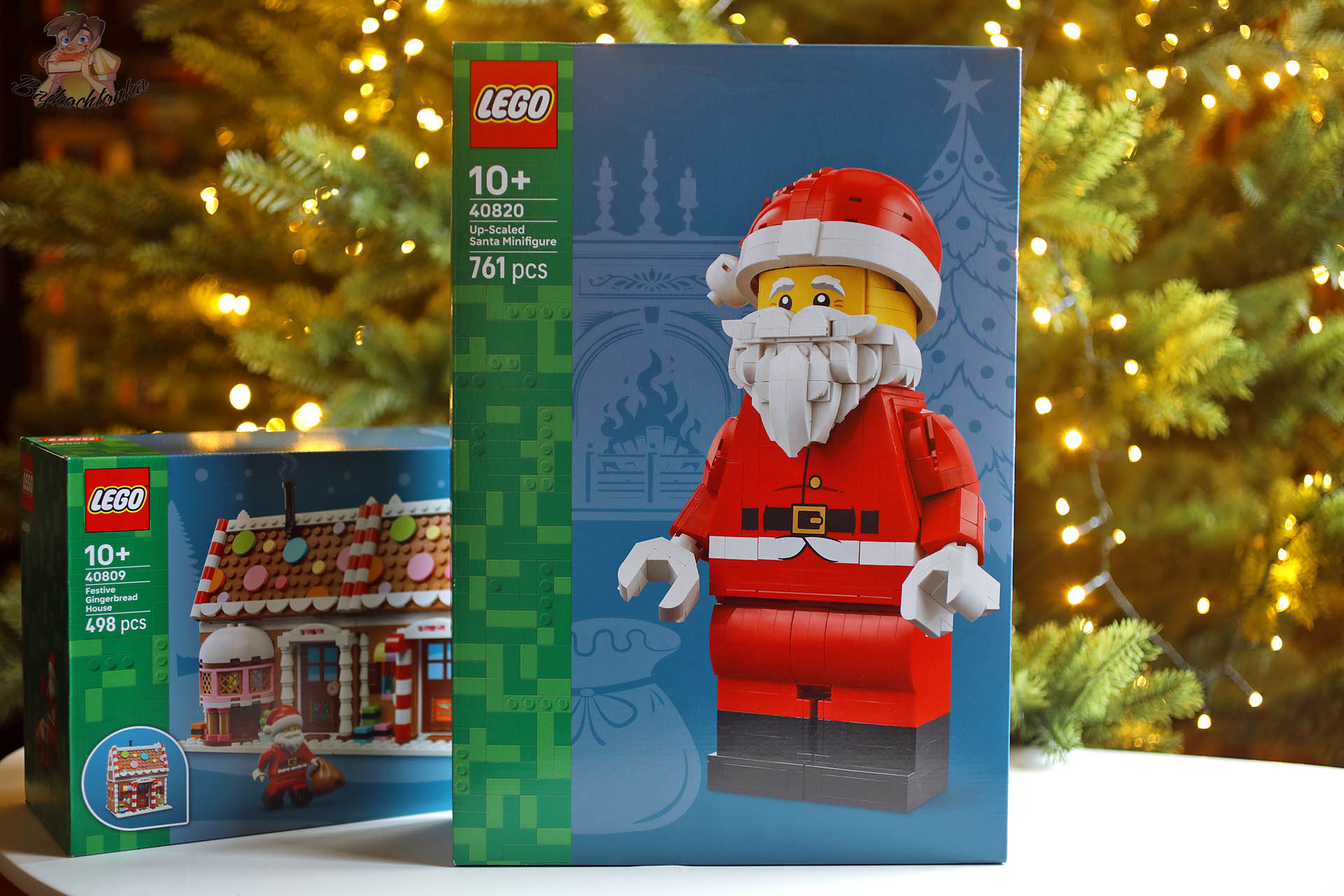 Pudełko LEGO 40820 Powiększona minifigurka Świętego Mikołaja obok zestawu LEGO 40809 Świąteczny domek z piernika