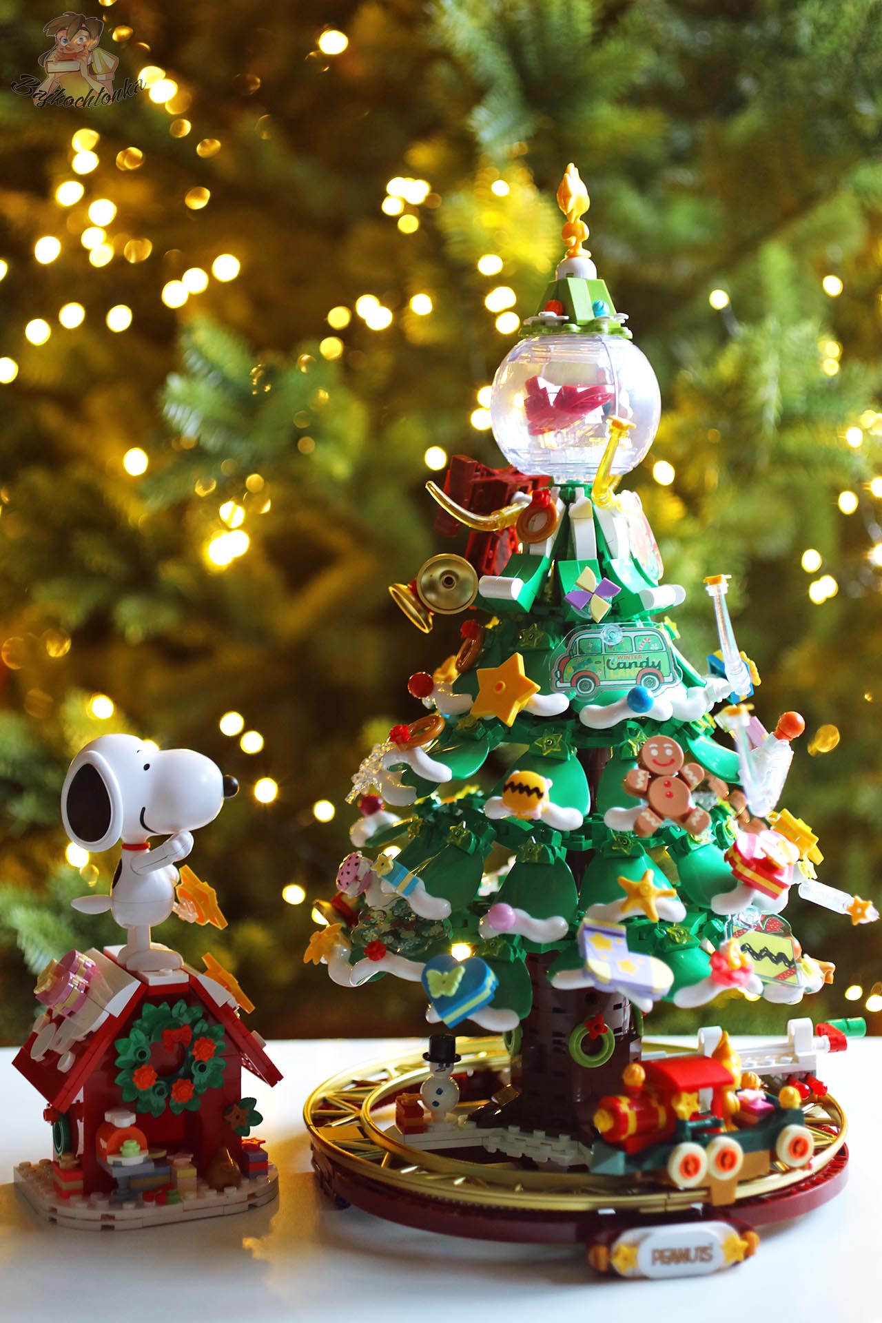 Choinka z klocków Pantasy Peanuts Christmas Tree 86909 z dużą figurką Snoopy’ego, pociągiem i bogatymi ozdobami, na tle świątecznych lampek.