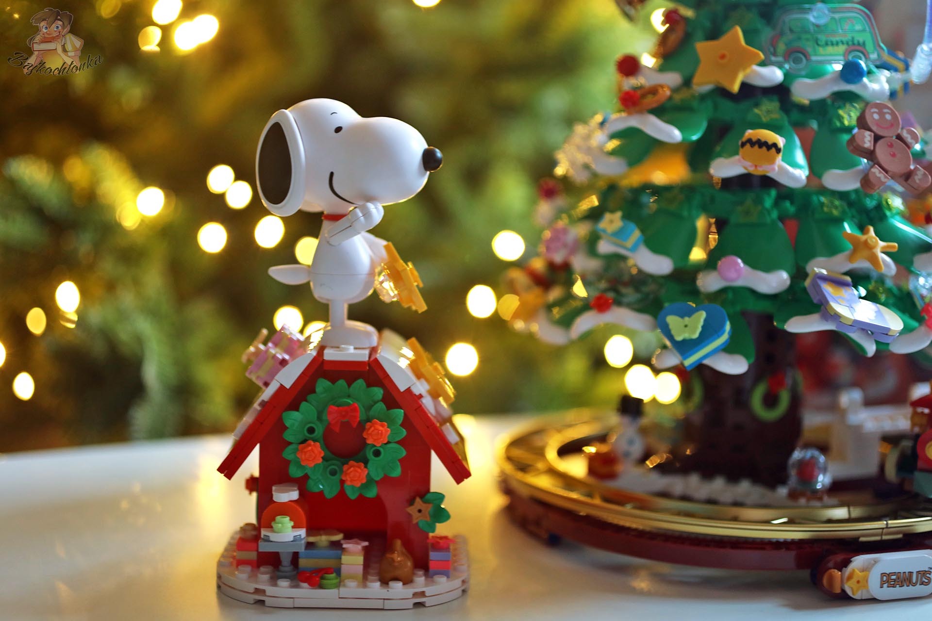 Duża figurka Snoopy’ego stojąca na ozdobionym świątecznie domku, obok choinki Pantasy Peanuts Christmas Tree.