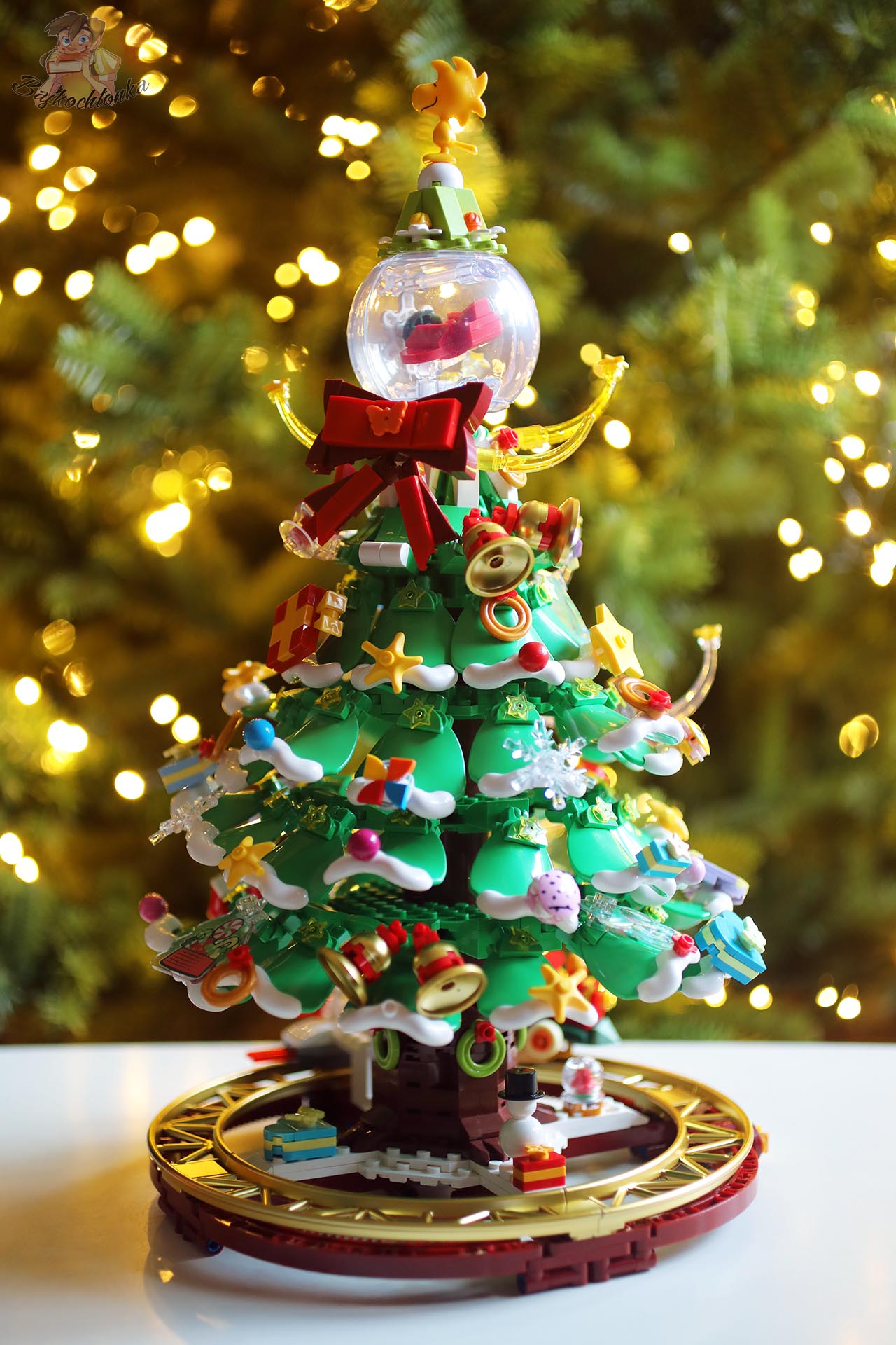Górna część choinki Pantasy Peanuts Christmas Tree z kulą śnieżną, Woodstockiem i czerwonymi kokardami, w świątecznej aranżacji.