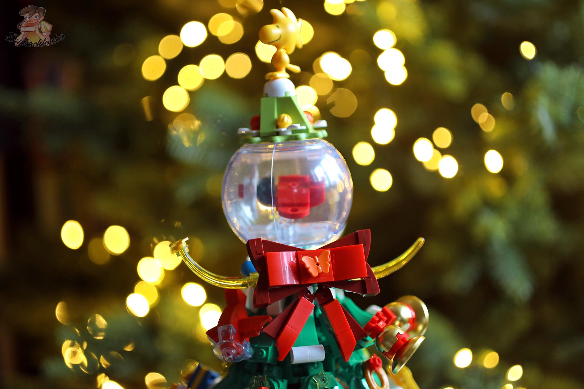 Figurka Woodstocka na czubku choinki Pantasy Peanuts Christmas Tree 86909, z przezroczystą kulą i świątecznym tłem.