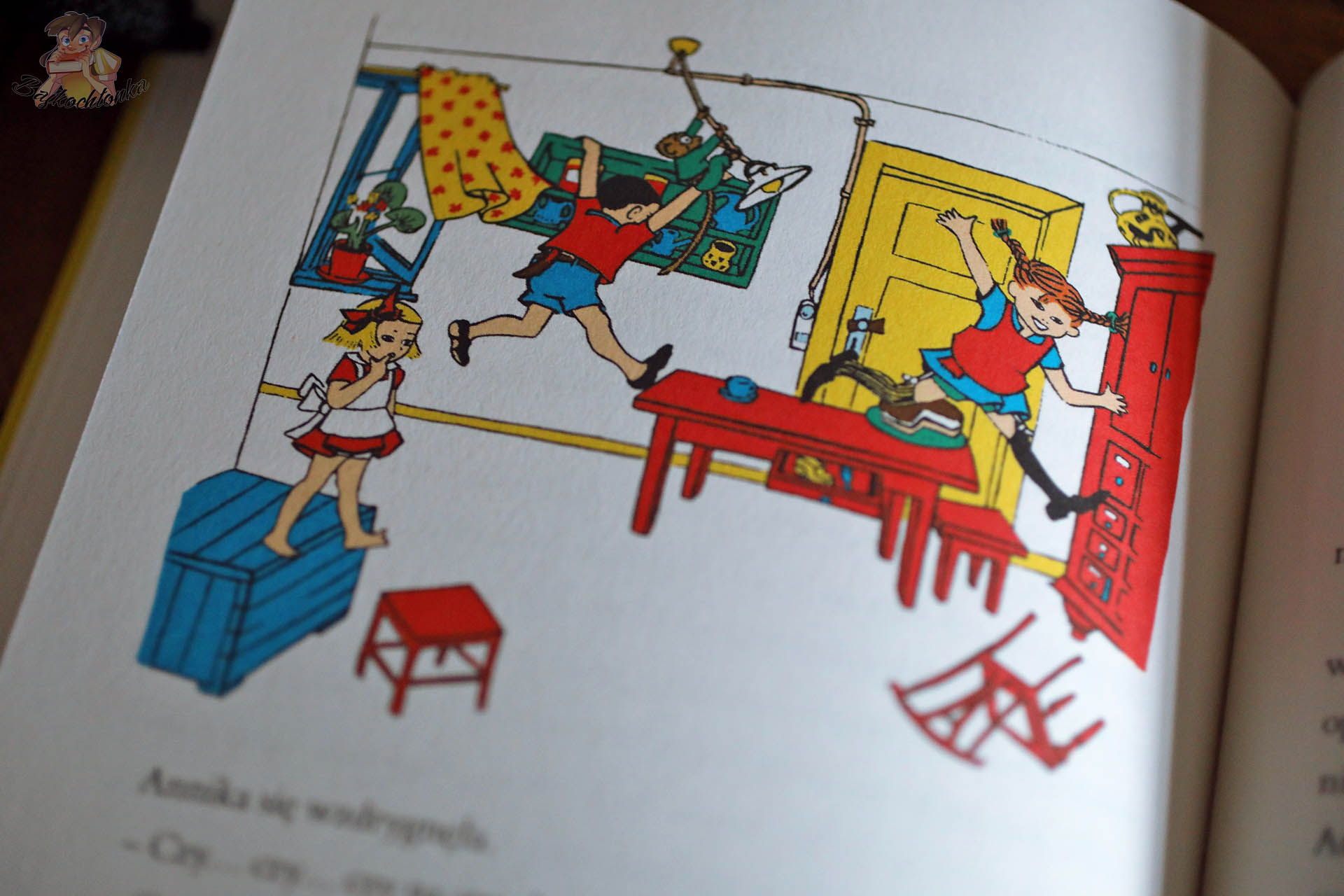 Kolorowa ilustracja z książki Pippi Pończoszanka, na której Pippi i dzieci biegają i skaczą po pokoju, przewracając meble i tworząc wesoły chaos.