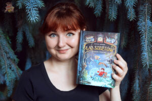 Autorka recenzji Bajkochłonka trzyma książkę Zaginiony profesor. Las Szeptów. Tom 2 w klimatycznej leśnej aranżacji