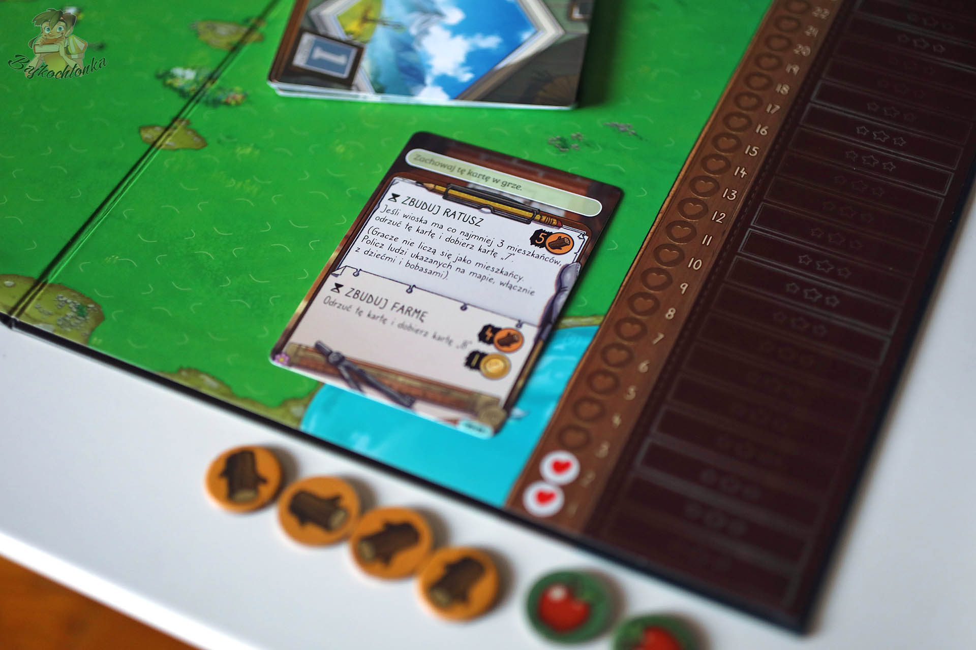 Elementy gry Naklejkowo – karta budowy ratusza i zasoby na planszy