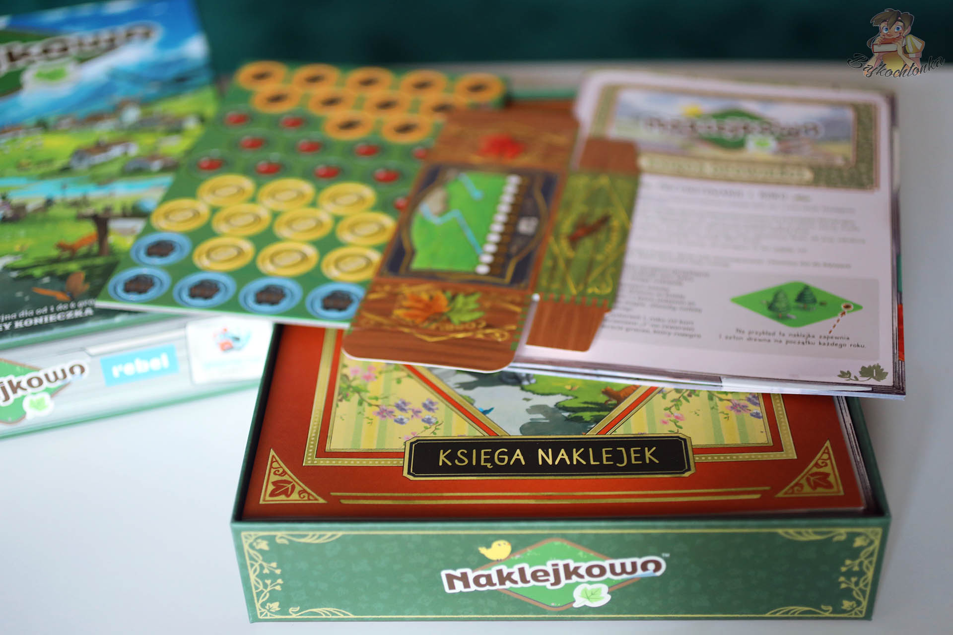 Księga naklejek i żetony zasobów w grze planszowej Naklejkowo
