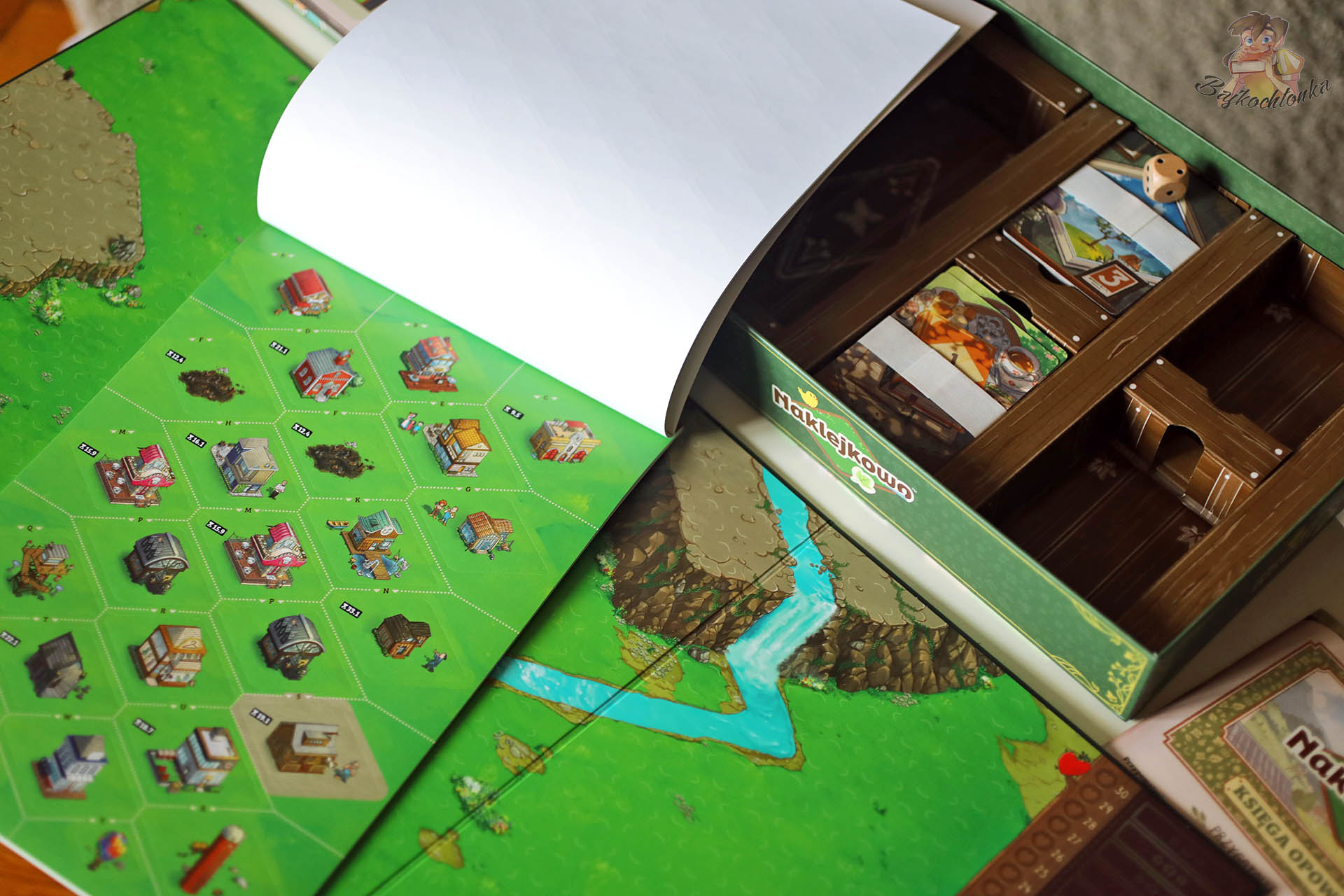 Zawartość pudełka gry Naklejkowo – plansza, talie kart, żetony i księga naklejek
