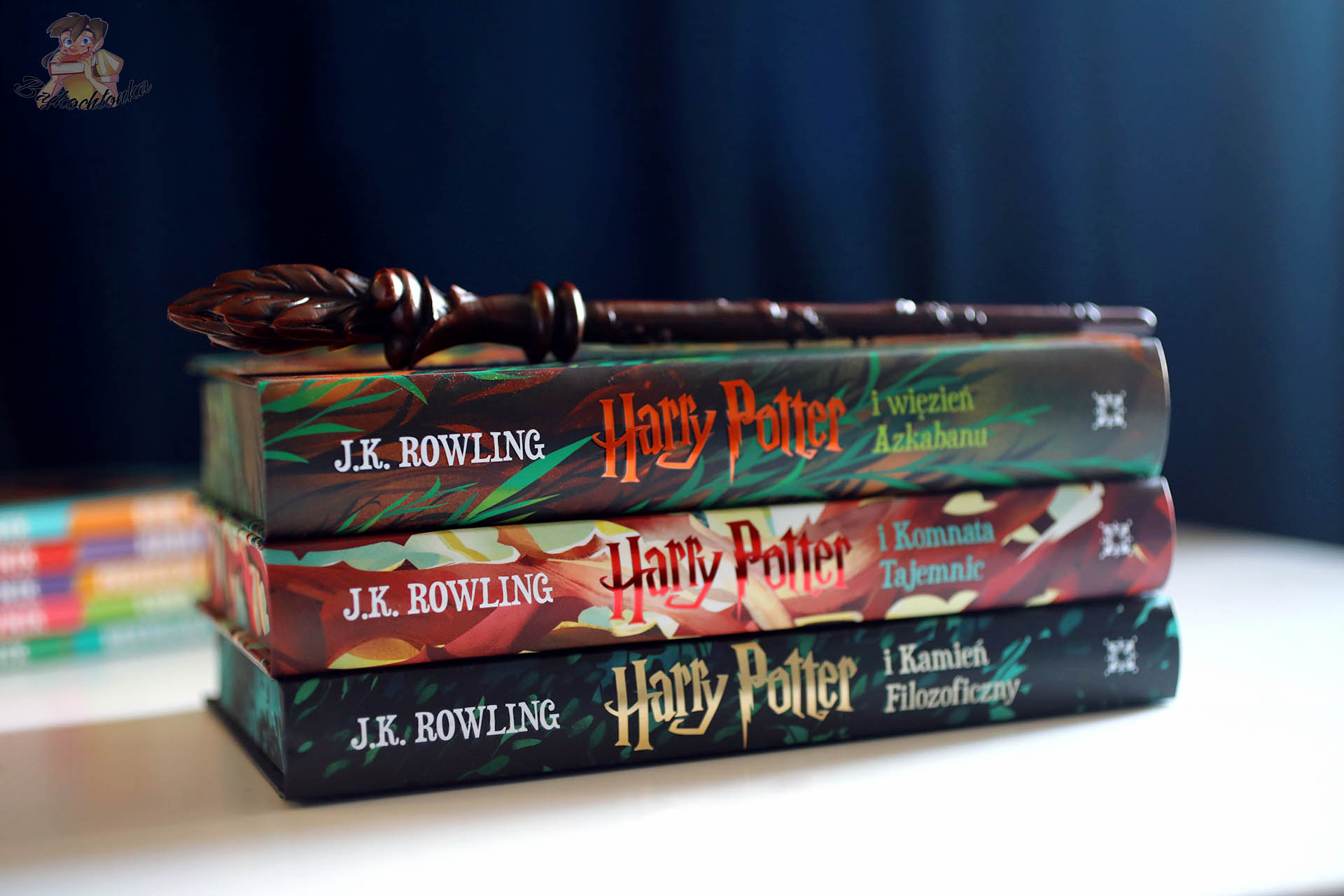 Grzbiety pierwszych trzech polskich wydań Harry’ego Pottera ułożonych w stos z różdżką na wierzchu