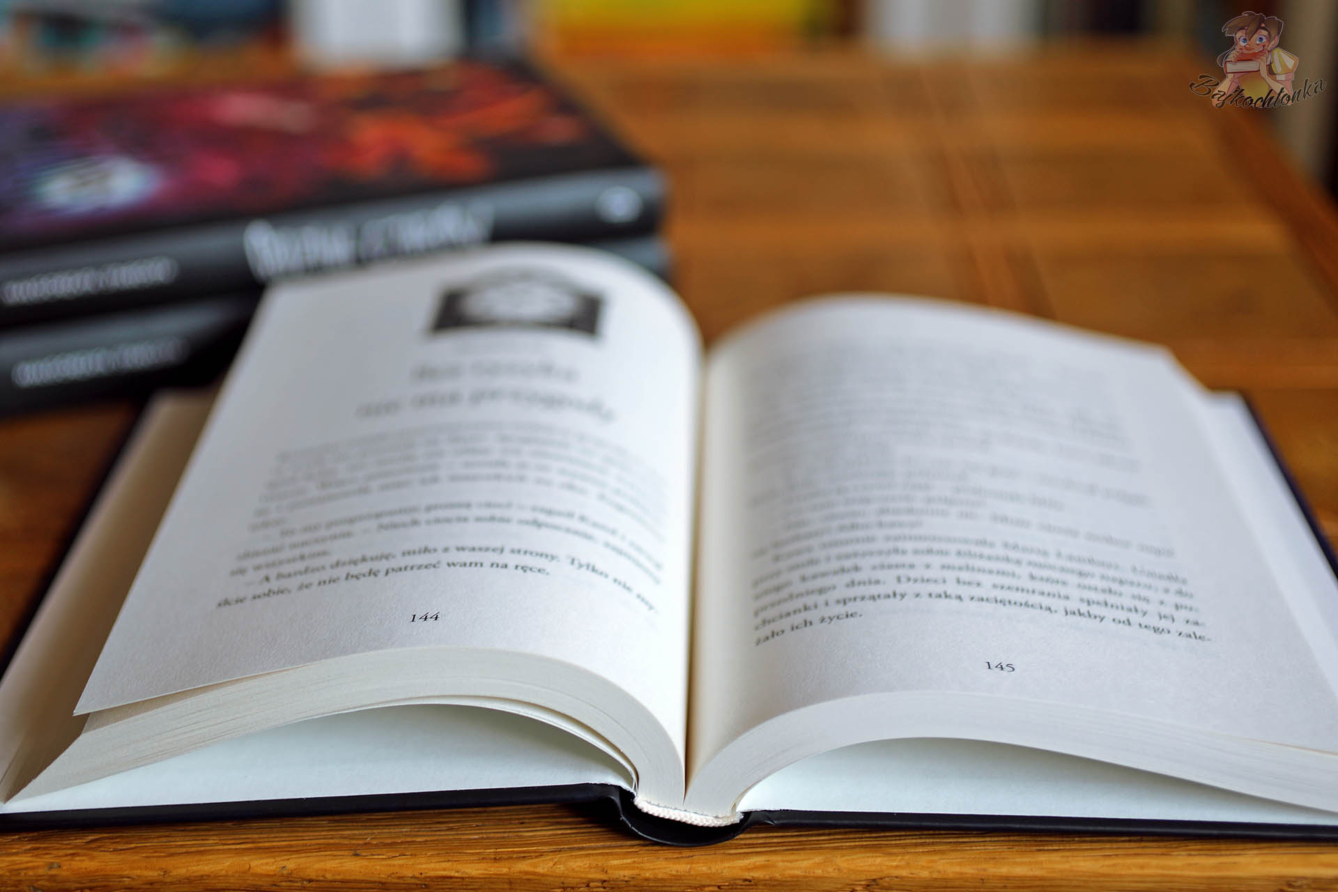 Otwarta książka Sekretny pokój Małgorzaty Starosty na stole, na tle tomów Godzina czarów i Zaklęte Miasteczko