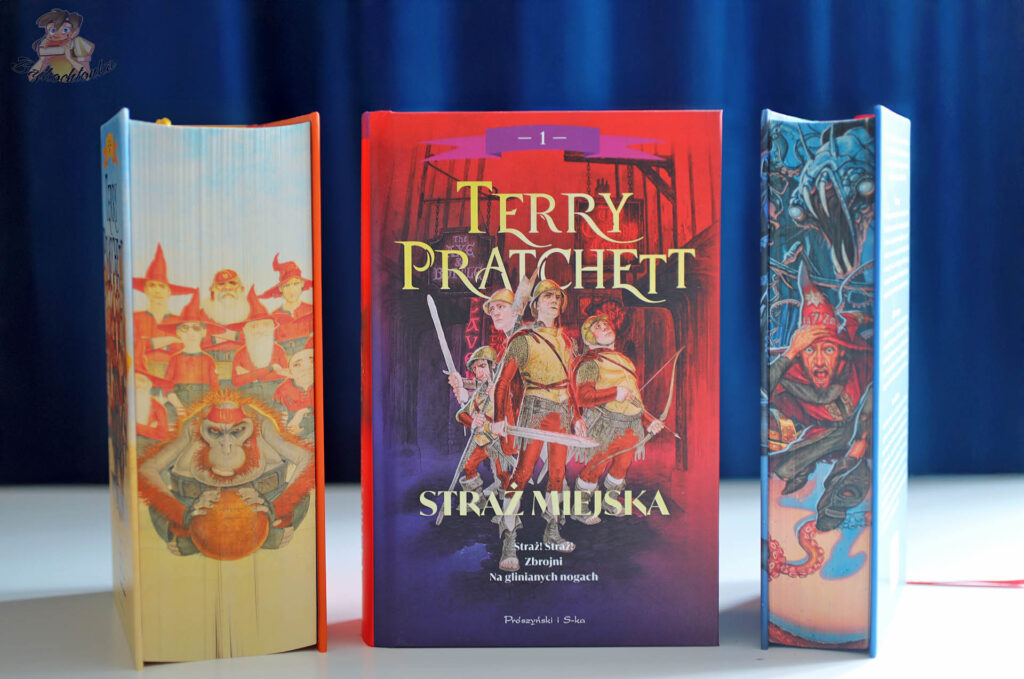 Okładka książki Straż miejska. Tom 1 (barwione brzegi) Terry’ego Pratchetta na tle tomów Rincewind