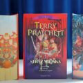 Okładka książki Straż miejska. Tom 1 (barwione brzegi) Terry’ego Pratchetta na tle tomów Rincewind