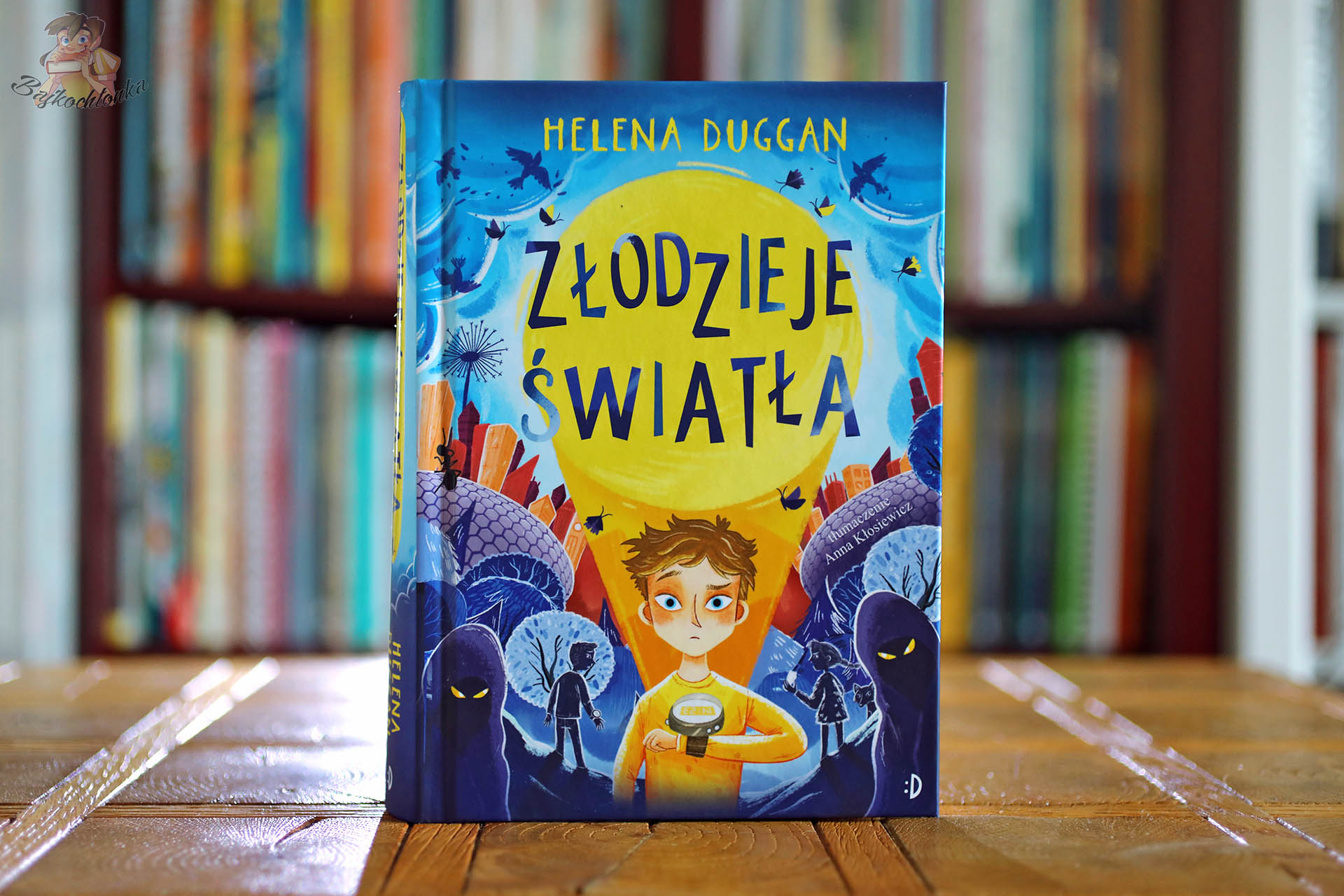 okładka książki Złodzieje światła Heleny Duggan na tle biblioteczki