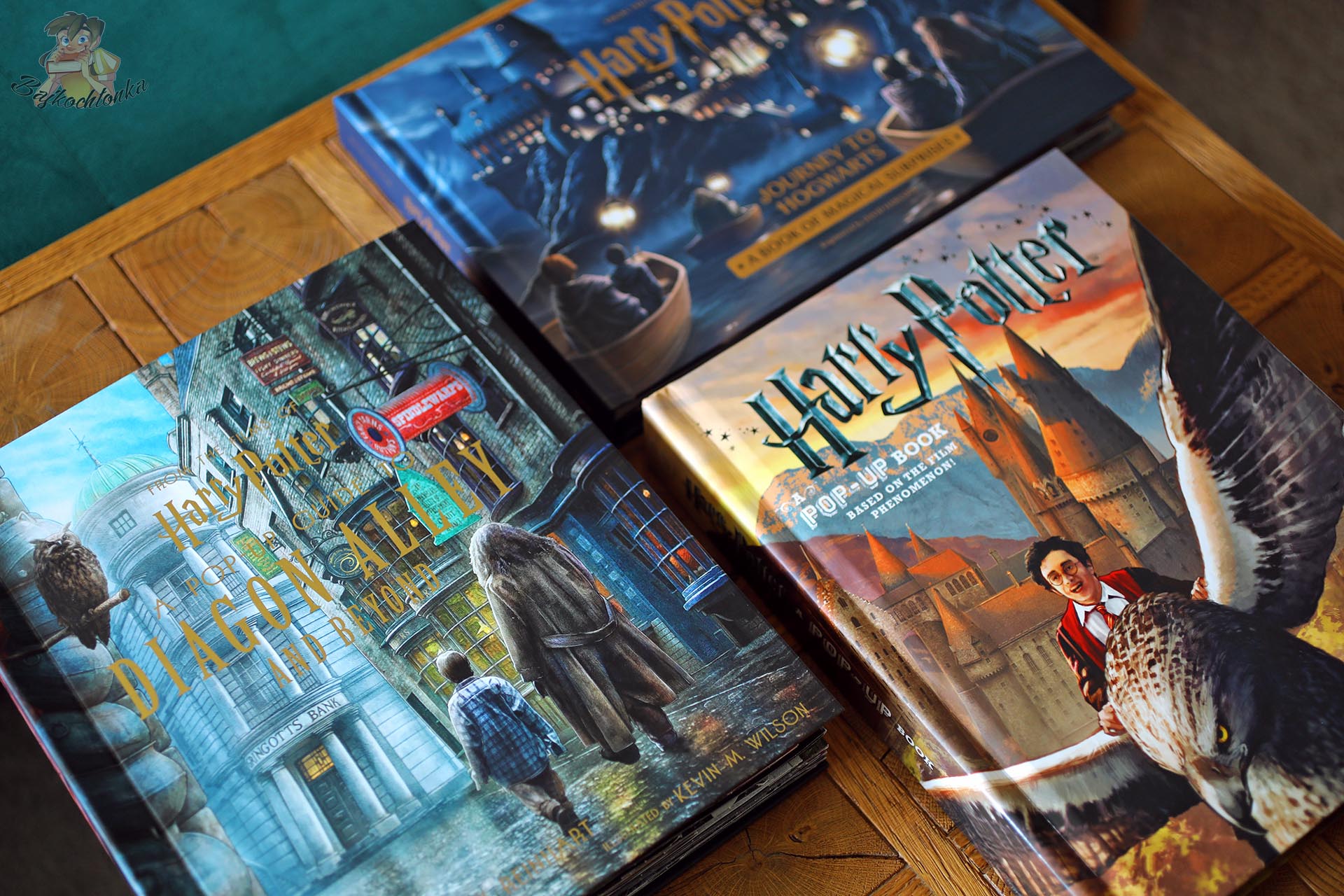 Książki pop-up ze świata Harry’ego Pottera, w tym Harry Potter’s Journey to Hogwarts od Insight Editions, ułożone na drewnianym stole