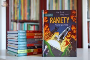 Okładka książki Rakiety. Pokonać grawitację Anne Drozd i Jerzego Drozda z serii Naukomiks, stojąca obok innych tomów popularnonaukowych komiksów dla dzieci.