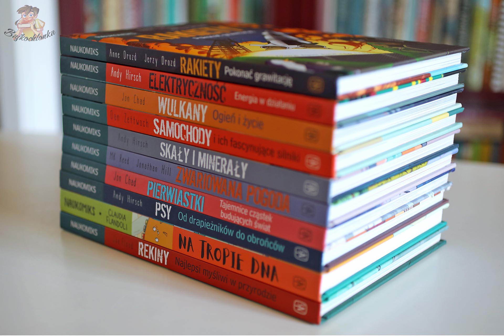 Stos książek z serii Naukomiks, w tym Rakiety, Elektryczność, Wulkany, Samochody, Skały i minerały, Zwariowana pogoda, Pierwiastki, Psy, Na tropie DNA i Rekiny.