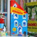 Okładka książki W domu Muminków z otwieranymi okienkami, stojąca obok muminkowej figurki i książki pop-up