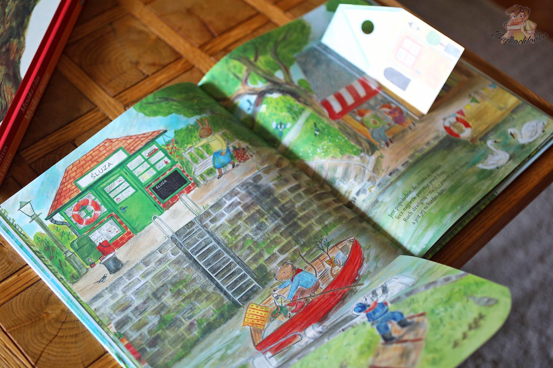 Ilustracja ze śluzą, łódką i otwartymi klapkami w książce Myszka nad rzeką