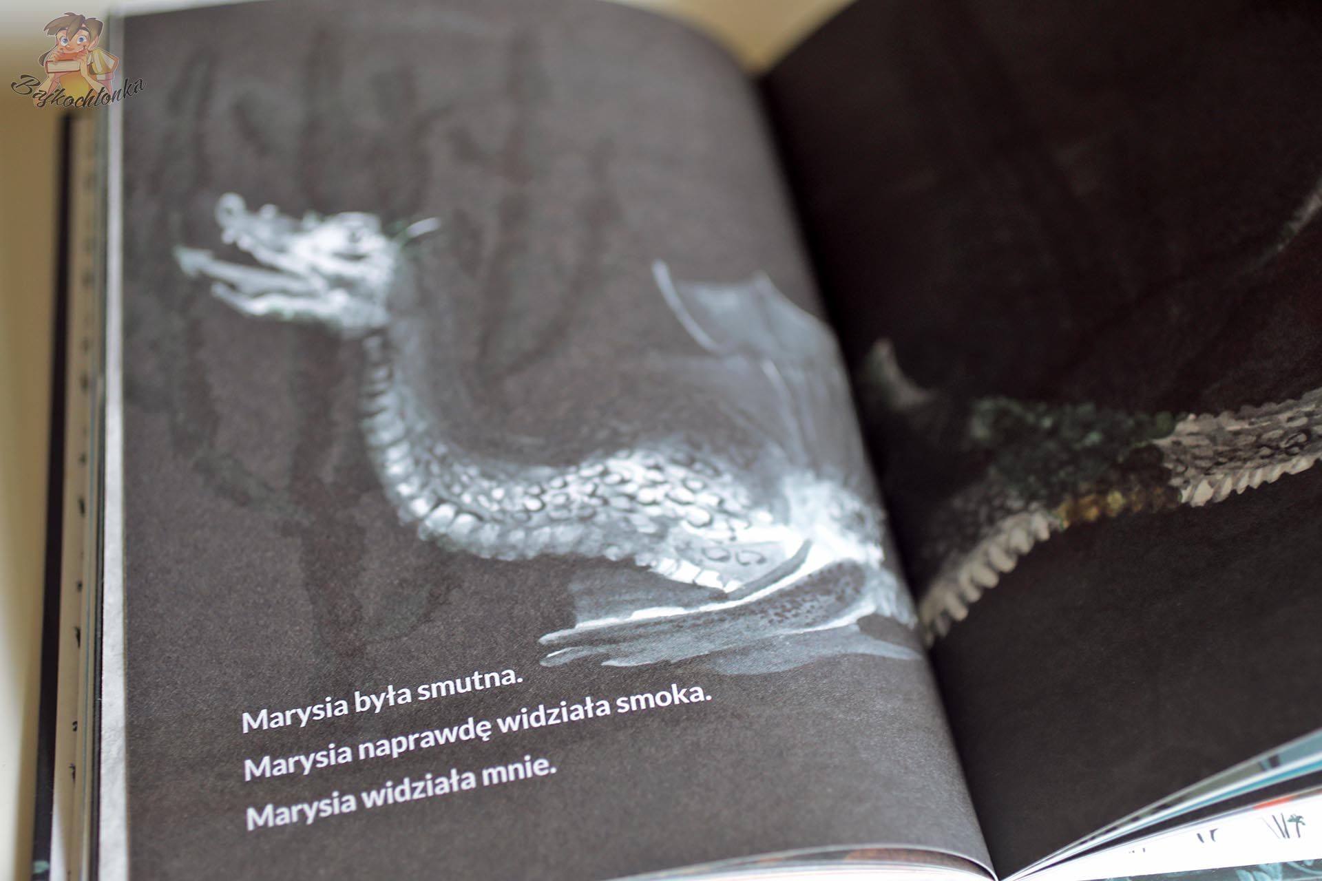 Strona z książki Smok z tekstem „Marysia naprawdę widziała smoka” i ciemną ilustracją smoka