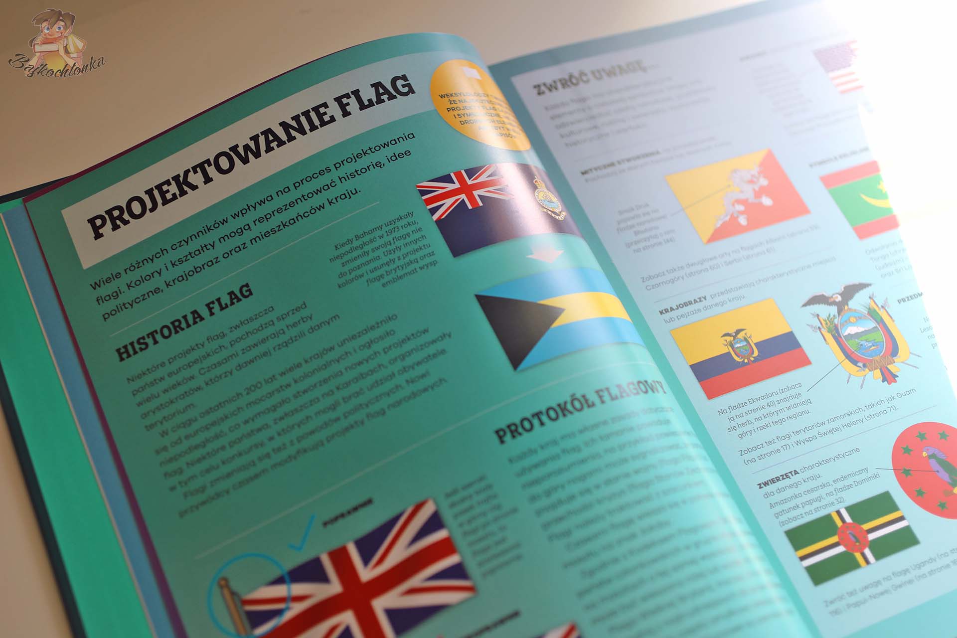 Zbliżenie na strony książki Flagi pokazujące zasady projektowania flag oraz symbole zwierząt, roślin i historyczne wzory narodowe.