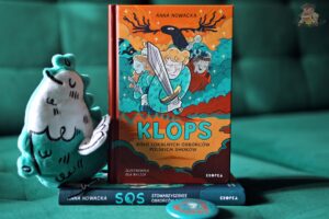 KLOPS. Koło Lokalnych Obrońców Polskich Smoków Anny Nowackiej – okładka książki z ilustracją Oli Bylicy, obok pluszowy smok i pierwszy tom SOS.