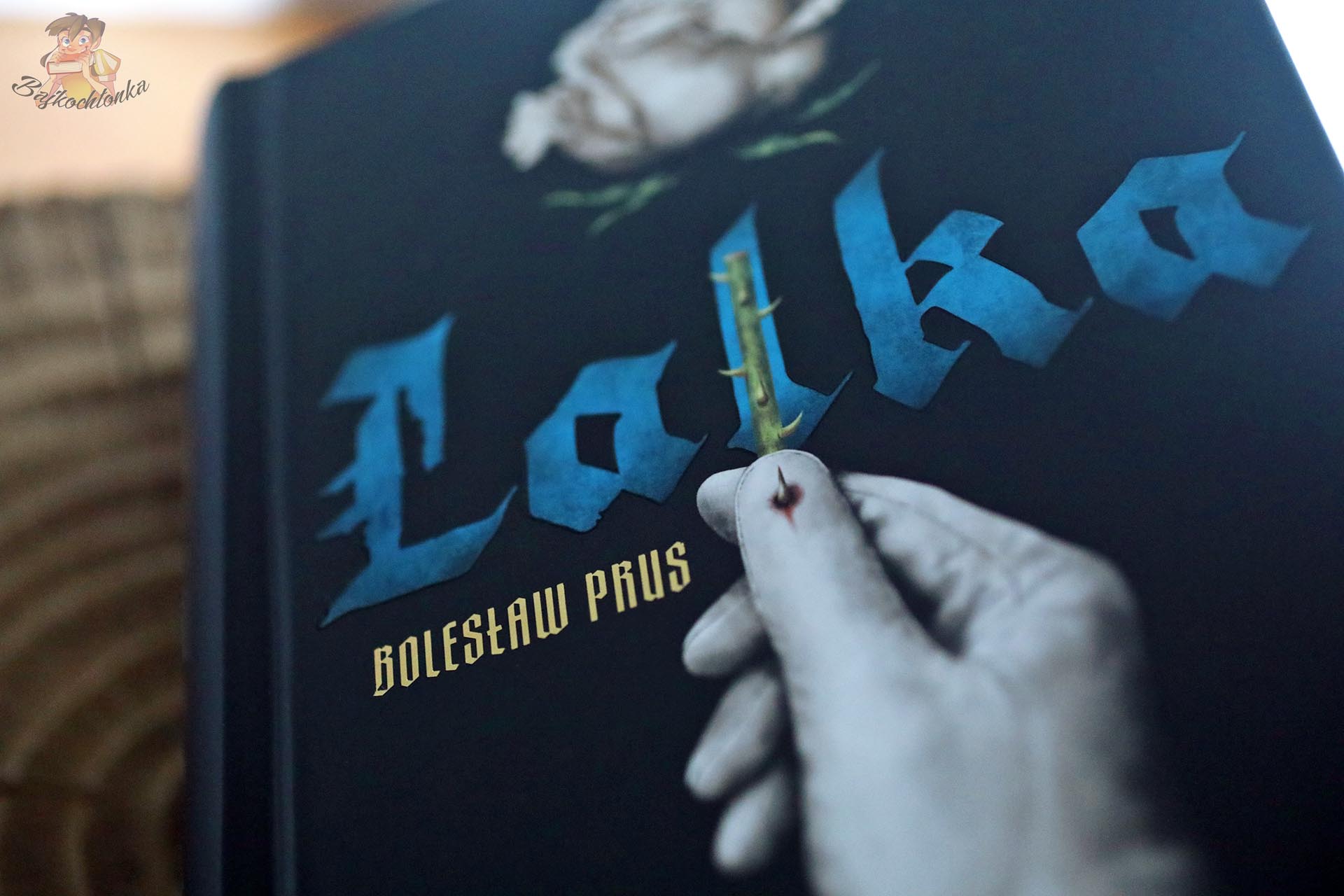 Detal okładki filmowego wydania Lalki z dłonią trzymającą łodygę róży